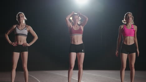 Three-women-athletes-prepare-for-a-track-race-in-a-dark-stadium-with-streetlights-on.-Time-lapse-footage-of-warm-up-and-concentration-of-a-group-of-women-before-the-race-on-the-track
